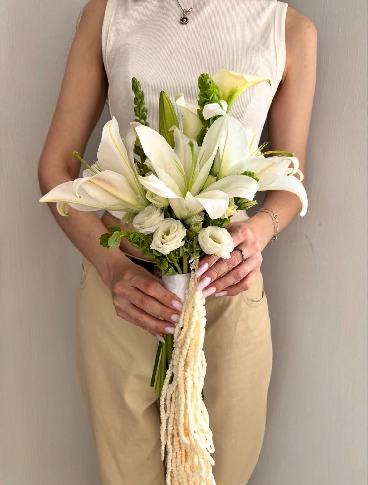 Luxury contemporary presentation bouquet featuring large white lilies, white lisianthus, green snapdragons, and long trailing white amaranthus held by a person by Lapin Flowers. Premium elite floral design for Washington DC, Bethesda, and Potomac MD.
