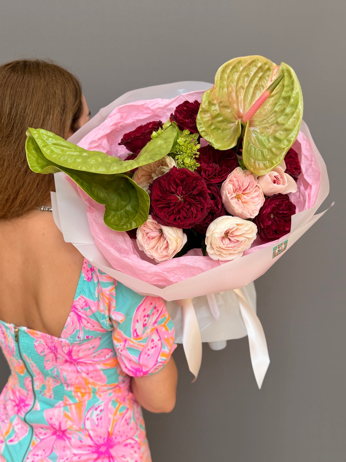 Extra-large luxury couture bouquet with deep crimson garden roses, blush pink roses, and large chartreuse-green anthuriums wrapped in a voluminous pink and white cloud wrap held by a woman by Lapin Flowers. Premium elite flower delivery for McLean VA, Potomac MD, and Washington DC.