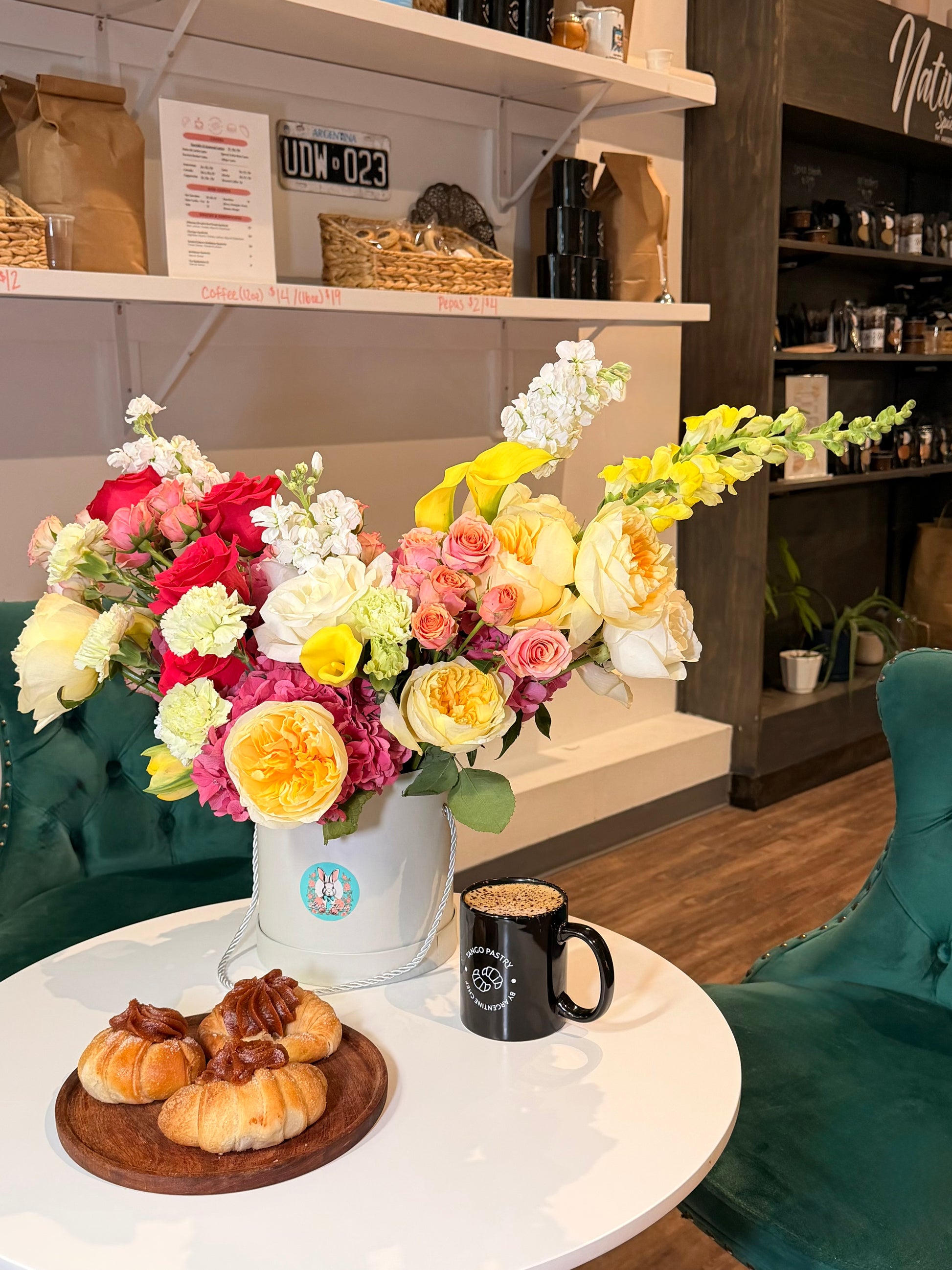 Extra-large luxury floral arrangement in a white signature hat box with yellow garden roses, yellow snapdragons, and a magenta hydrangea on a white cafe table with coffee by Lapin Flowers. Premium elite floral delivery for Potomac MD and Washington DC.⁠