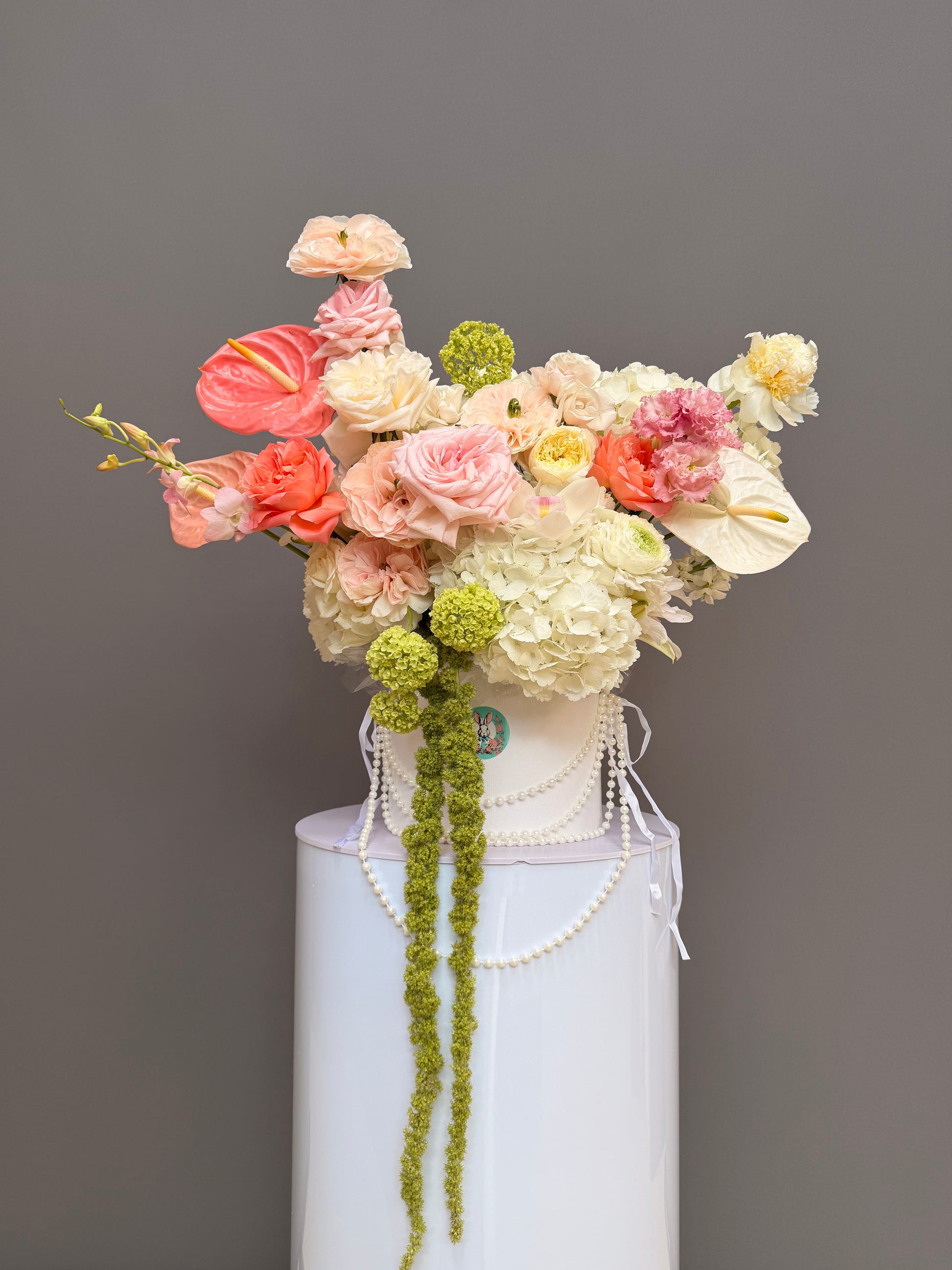 Luxury couture flower arrangement in a hat box with anthuriums, hydrangea, garden roses, cascading amaranthus, and pearls by Lapin Flowers, premium florist serving Bethesda MD, Potomac, and Washington DC.⁠