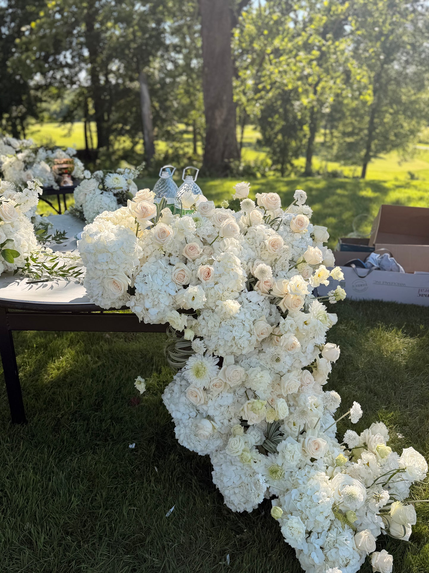 Grand luxury wedding floral installation featuring a dense table runner with white hydrangeas and blush roses cascading down onto the grass by Lapin Flowers. Premium elite event design expertly curated for Washington DC, Potomac, Bethesda, Rockville, and the historic waterfront estates of Annapolis, Maryland. Serving the premier corporate hubs and high-end residential enclaves of Northern Virginia, including Tysons, McLean, Great Falls, Arlington, and Alexandria.