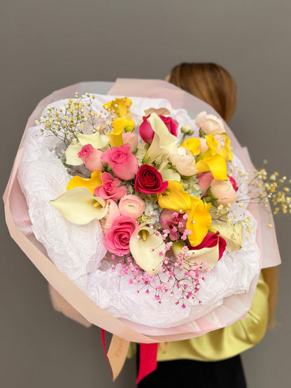Large luxury mixed bouquet with yellow calla lilies, white calla lilies, magenta roses, and ranunculus wrapped in a big white tissue cloud held by a person by Lapin Flowers. Premium elite event floral design for Washington DC and Potomac MD, McLean VA, Bethesda MD, Annapolis MD. 