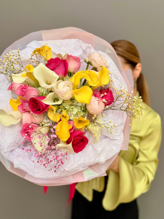 Large luxury mixed bouquet with yellow calla lilies, white calla lilies, magenta roses, and ranunculus wrapped in a big white tissue cloud held by a person by Lapin Flowers. Premium elite event floral design for Washington DC and Potomac MD, McLean VA, Bethesda MD, Annapolis MD. 
