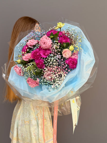 Person holding a Extra-large luxury artisan flower bouquet with tinted blue and pink gypsophila, magenta carnations, and pink lisianthus wrapped in ice-blue paper by Lapin Flowers. Upscale grand delivery for Washington DC, Maryland, and Virginia.