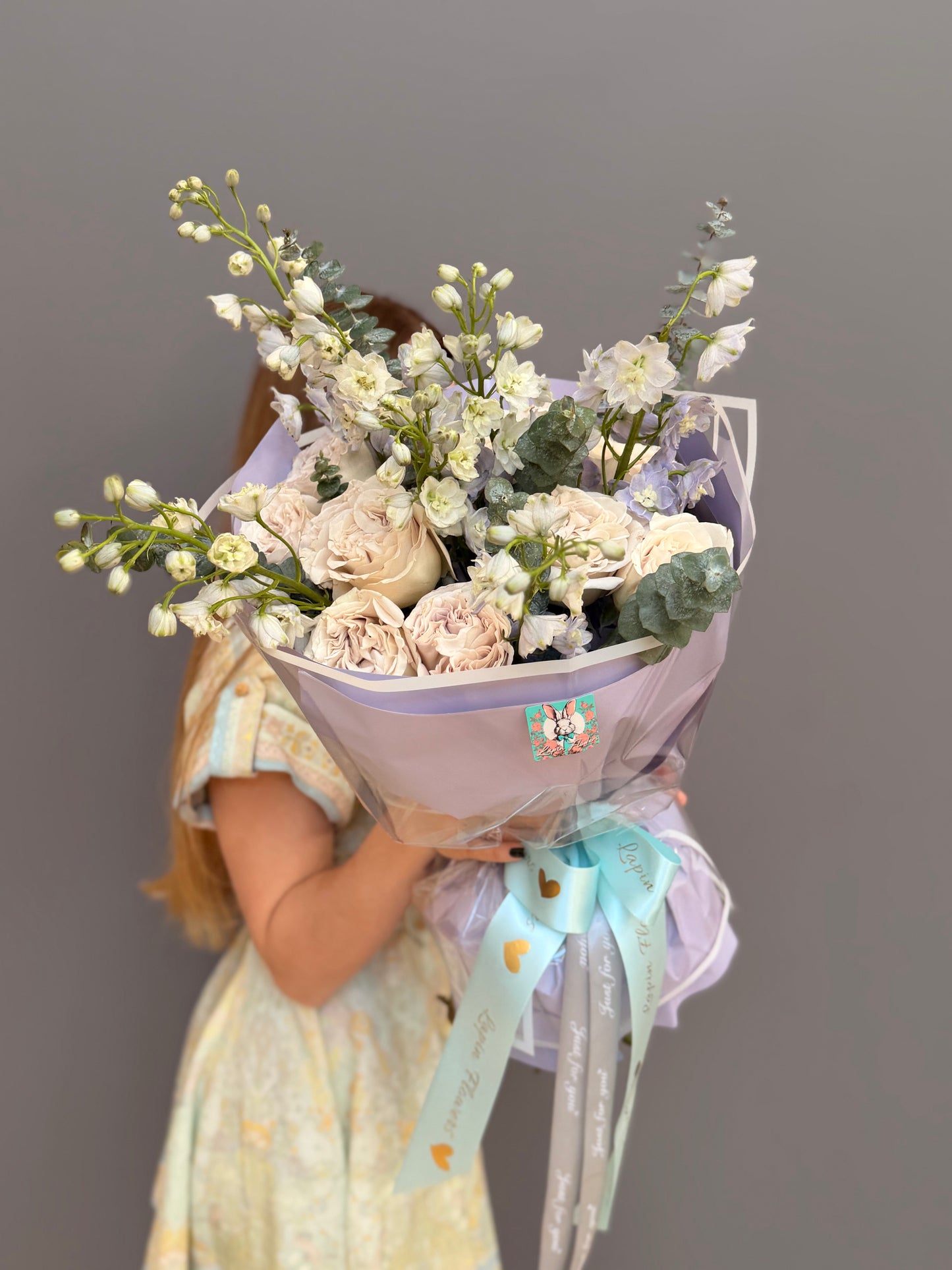 Luxury couture flower bouquet featuring Westminster Abbey sand-beige garden roses, white delphinium, and eucalyptus by Lapin Flowers. Upscale floral art in lavender wrapping paper for delivery in Northern Virginia, Washington DC, and Maryland.⁠