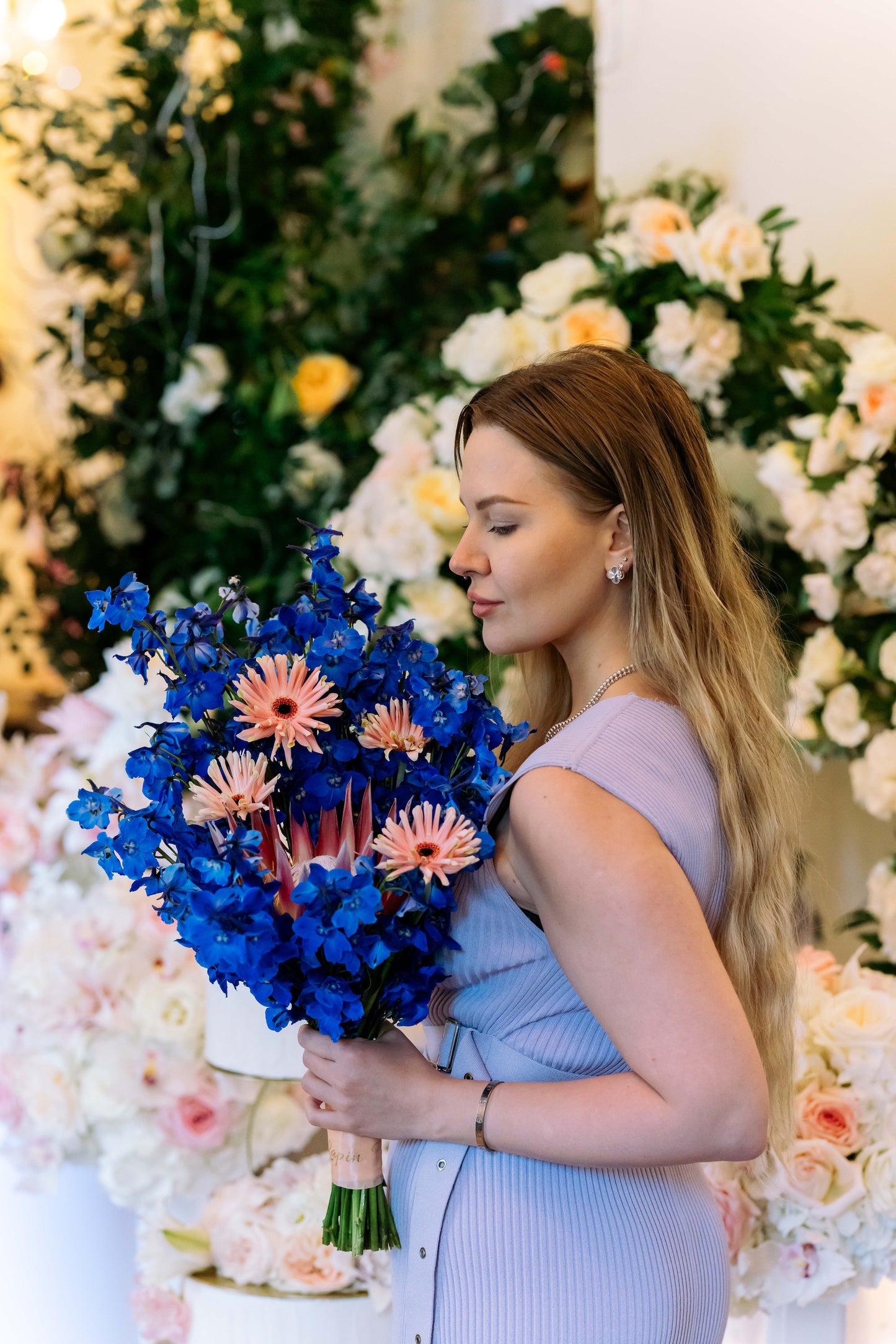 Luxury contemporary artisan bouquet with a large pink King Protea, blush spider gerberas, and a dramatic cloud of electric blue delphinium held by a florist by Lapin Flowers. Premium exotic flower delivery for Washington DC and Maryland.⁠