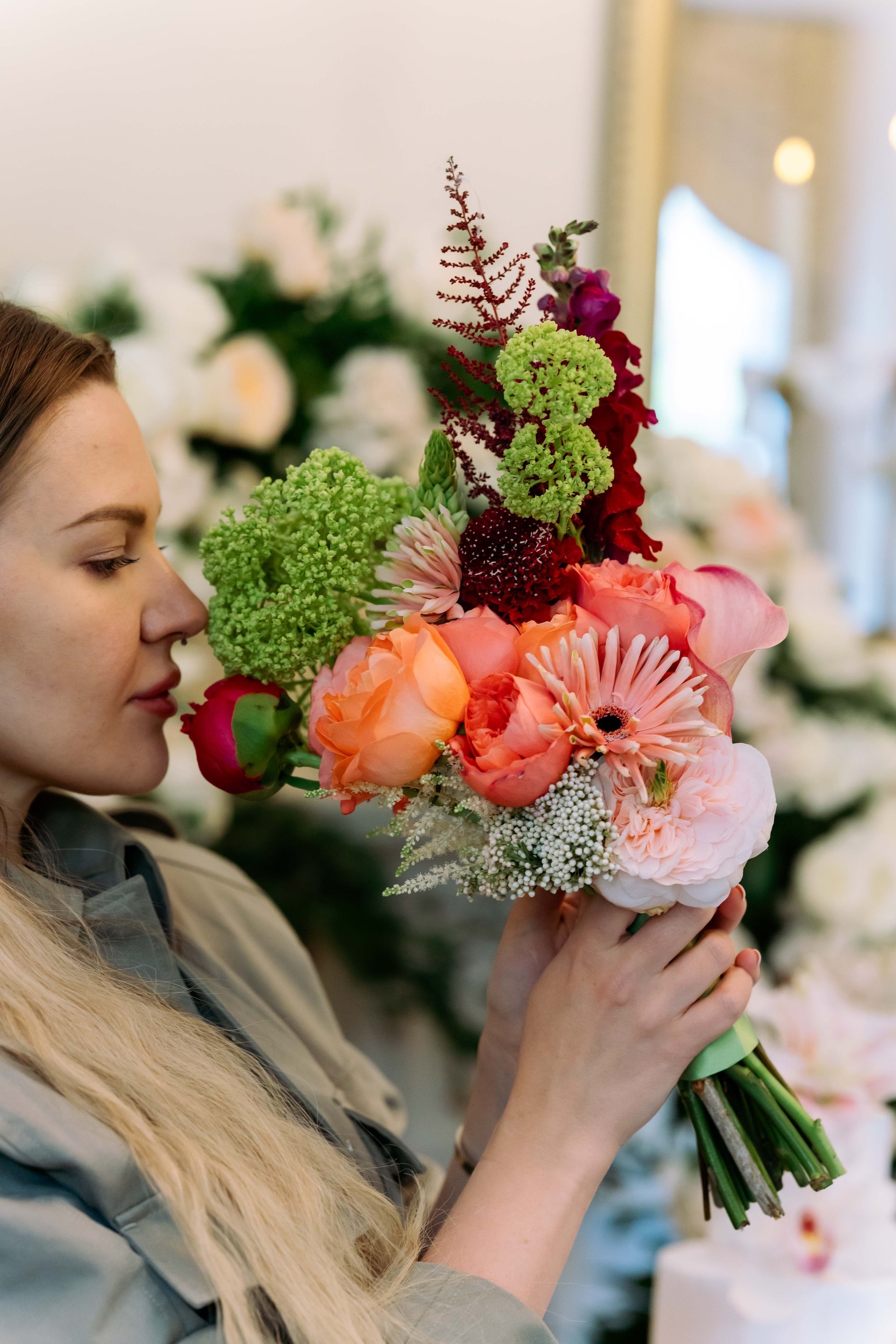 Luxury contemporary asymmetric bouquet with terracotta garden roses, a peach calla lily, burgundy snapdragons, and lime green trachelium held by a woman by Lapin Flowers. Premium elite floral delivery for Washington DC and Potomac Maryland.⁠