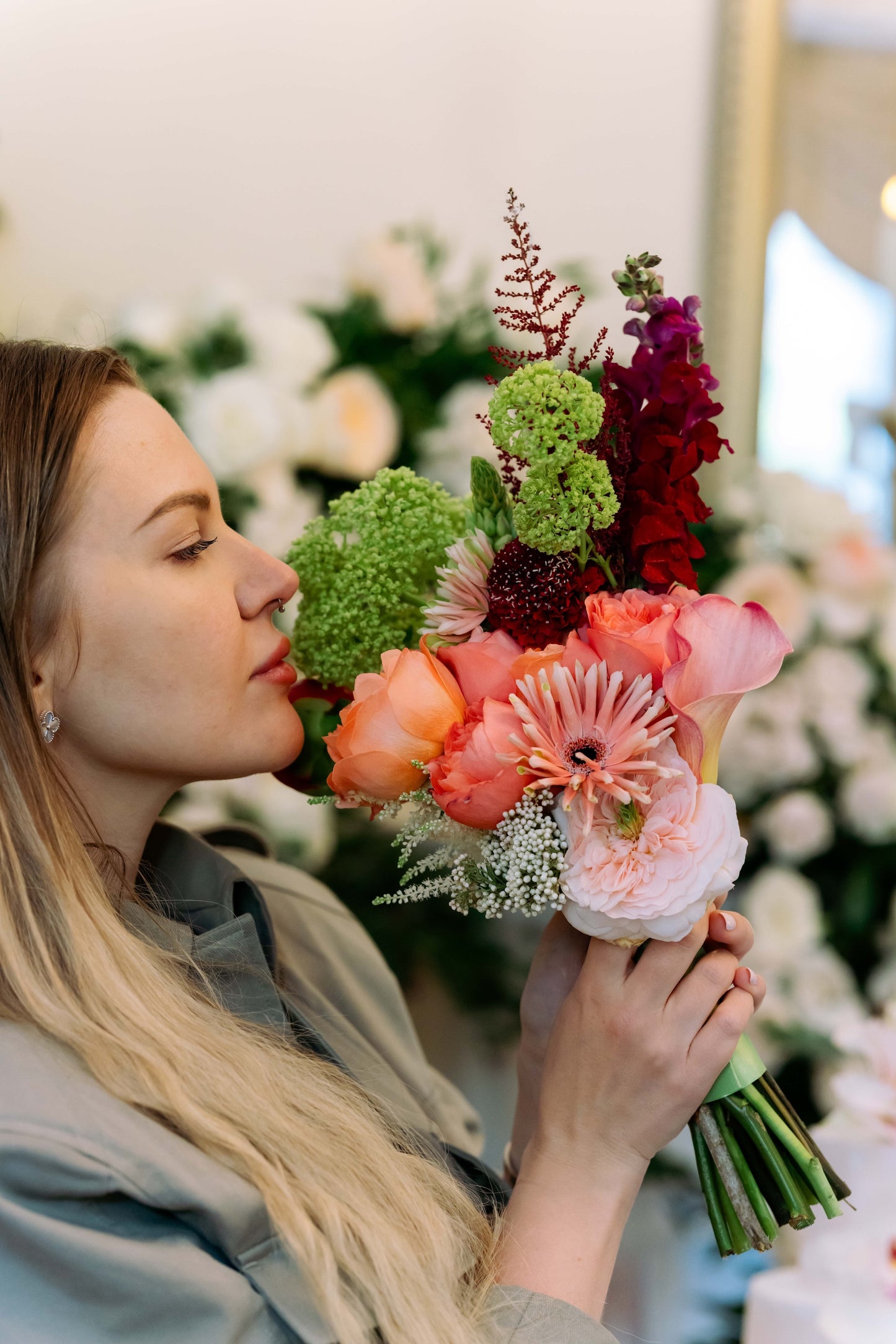Luxury contemporary asymmetric bouquet with terracotta garden roses, a peach calla lily, burgundy snapdragons, and lime green trachelium held by a woman by Lapin Flowers. Premium elite floral delivery for Washington DC and Potomac Maryland.⁠