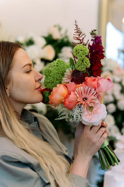 Luxury contemporary asymmetric bouquet with terracotta garden roses, a peach calla lily, burgundy snapdragons, and lime green trachelium held by a woman by Lapin Flowers. Premium elite floral delivery for Washington DC and Potomac Maryland.⁠