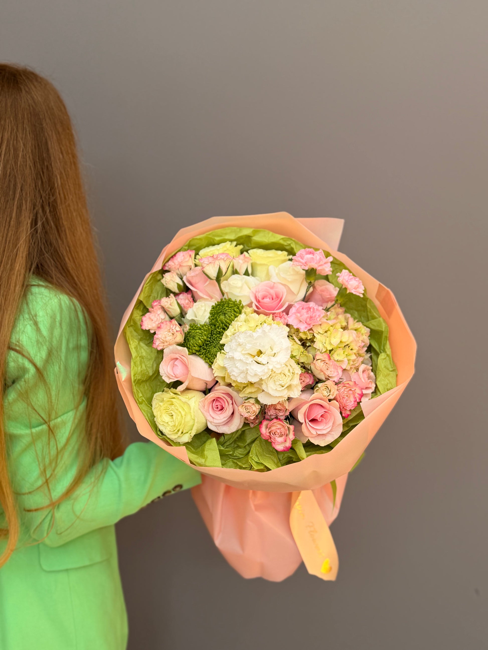Person is holding a Premium luxury artisan flower bouquet with pink roses, white lisianthus, lime-green hydrangea, and green button mums wrapped in peach and olive paper by Lapin Flowers. Upscale floral design for delivery in Maryland, Washington DC, and Northern Virginia.
