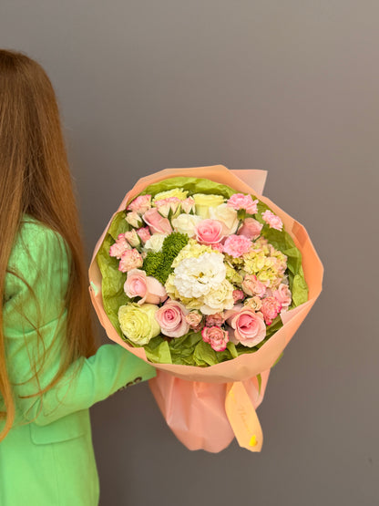 Person is holding a Premium luxury artisan flower bouquet with pink roses, white lisianthus, lime-green hydrangea, and green button mums wrapped in peach and olive paper by Lapin Flowers. Upscale floral design for delivery in Maryland, Washington DC, and Northern Virginia.
