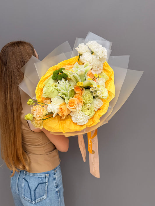Extra-large luxury artisan flower bouquet with peach roses, white lilies, white lisianthus, and green button mums wrapped in bright yellow and frosted paper by Lapin Flowers. Premium flower delivery for Washington DC and Maryland.⁠