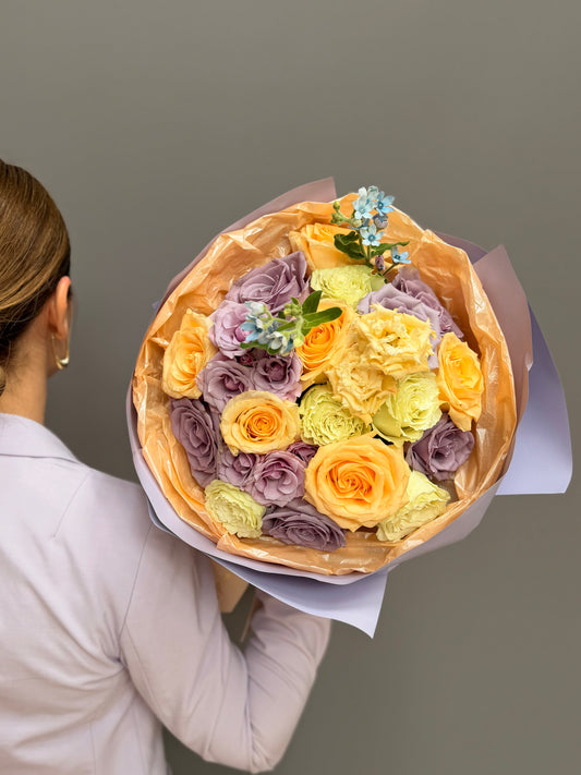 Person holding a extra-large luxury artisan flower bouquet with peach roses, white lilies, white lisianthus, and green button mums wrapped in bright yellow and frosted paper by Lapin Flowers. Premium flower delivery for Washington DC and Maryland.