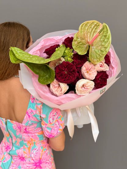 Extra-large luxury couture bouquet with deep crimson garden roses, blush pink roses, and large chartreuse-green anthuriums wrapped in a voluminous pink and white cloud wrap held by a woman by Lapin Flowers. Premium elite flower delivery for McLean VA, Potomac MD, and Washington DC.
