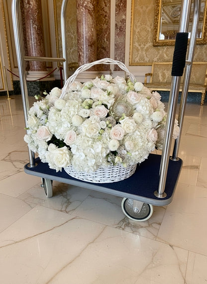 Basket of white flowers on a trolley in an elegant room with marble floors and ornate walls.