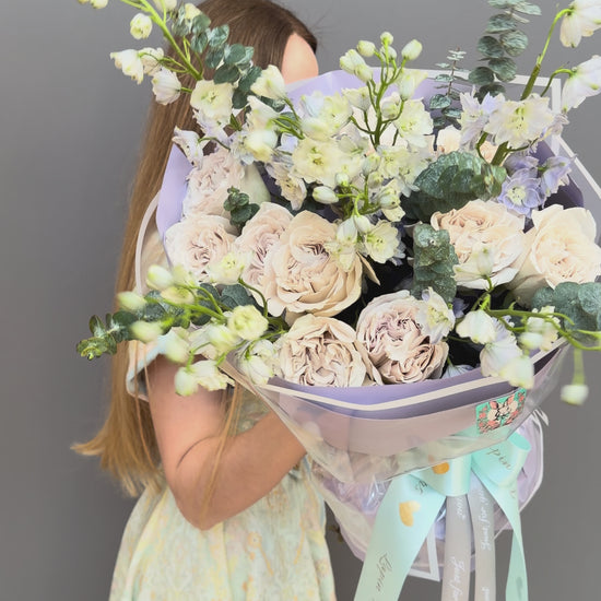 Luxury couture flower bouquet featuring Westminster Abbey sand-beige garden roses, white delphinium, and eucalyptus by Lapin Flowers. Upscale floral art in lavender wrapping paper for delivery in Northern Virginia, Washington DC, and Maryland.⁠