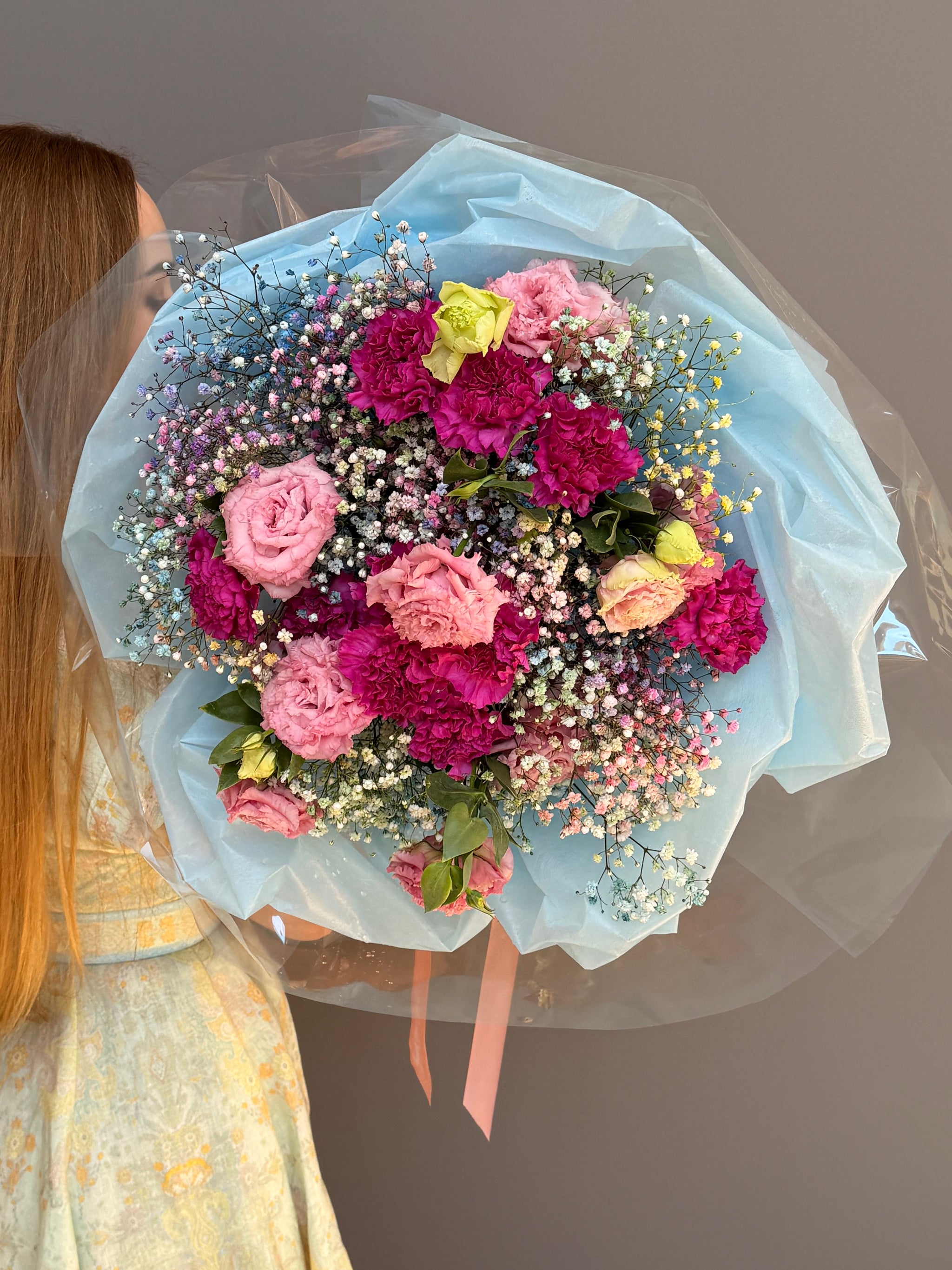 Person holding a Extra-large luxury artisan flower bouquet with tinted blue and pink gypsophila, magenta carnations, and pink lisianthus wrapped in ice-blue paper by Lapin Flowers. Upscale grand delivery for Washington DC, Maryland, and Virginia.