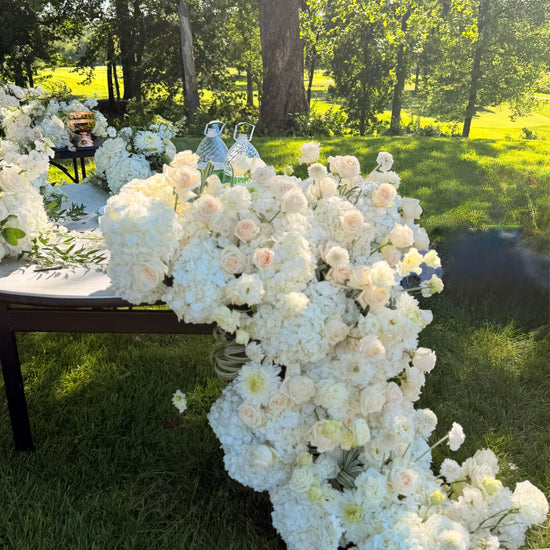 Grand luxury wedding floral installation featuring a dense table runner with white hydrangeas and blush roses cascading down onto the grass by Lapin Flowers. Premium elite event design expertly curated for Washington DC, Potomac, Bethesda, Rockville, and the historic waterfront estates of Annapolis, Maryland. Serving the premier corporate hubs and high-end residential enclaves of Northern Virginia, including Tysons, McLean, Great Falls, Arlington, and Alexandria.