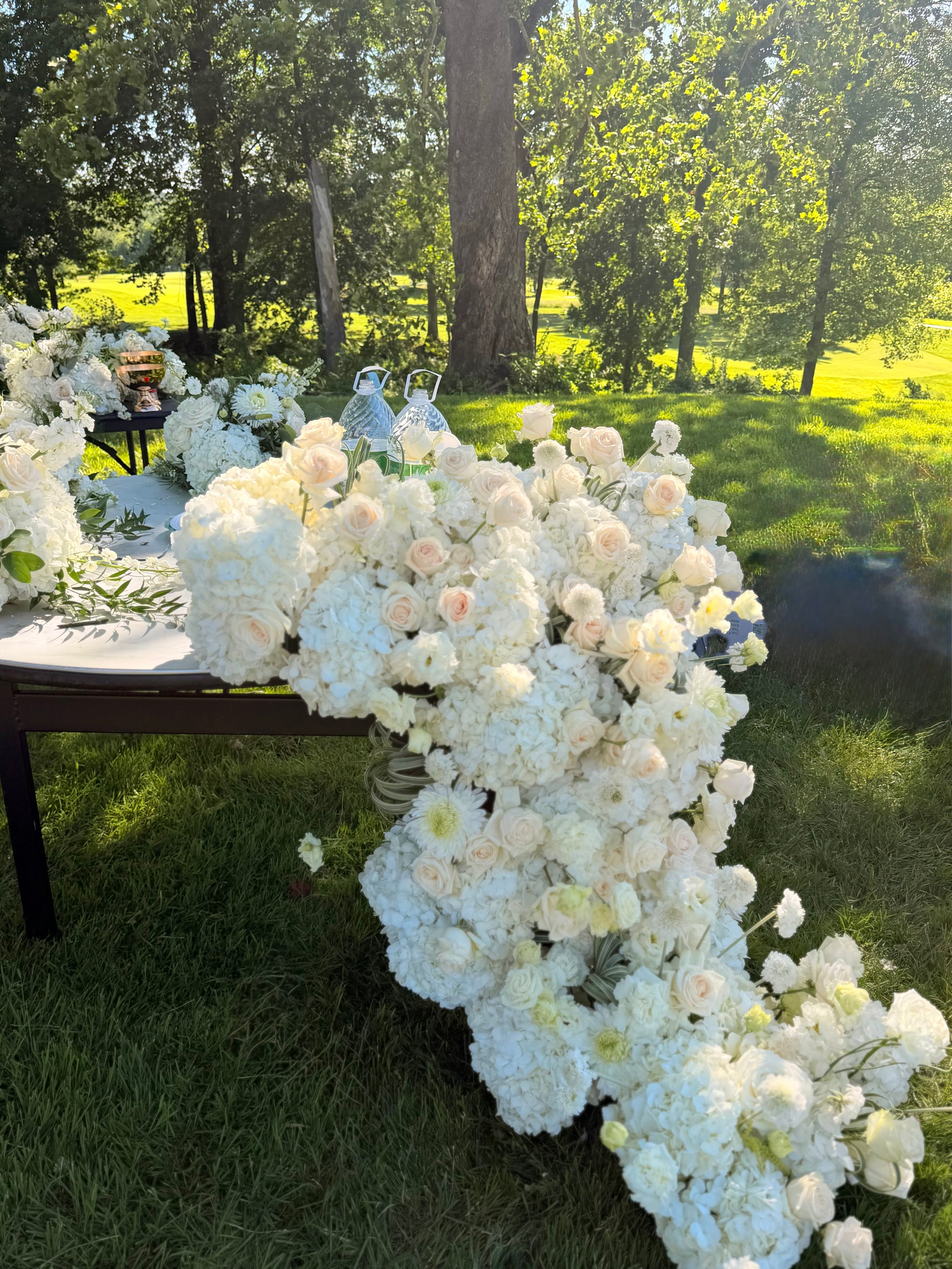 Grand luxury wedding floral installation featuring a dense table runner with white hydrangeas and blush roses cascading down onto the grass by Lapin Flowers. Premium elite event design expertly curated for Washington DC, Potomac, Bethesda, Rockville, and the historic waterfront estates of Annapolis, Maryland. Serving the premier corporate hubs and high-end residential enclaves of Northern Virginia, including Tysons, McLean, Great Falls, Arlington, and Alexandria.